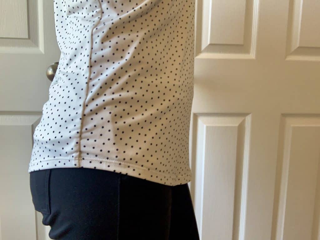 women with black pants and a white shirt with white polka dots demonstrating you cannot tell there is a fanny pack.