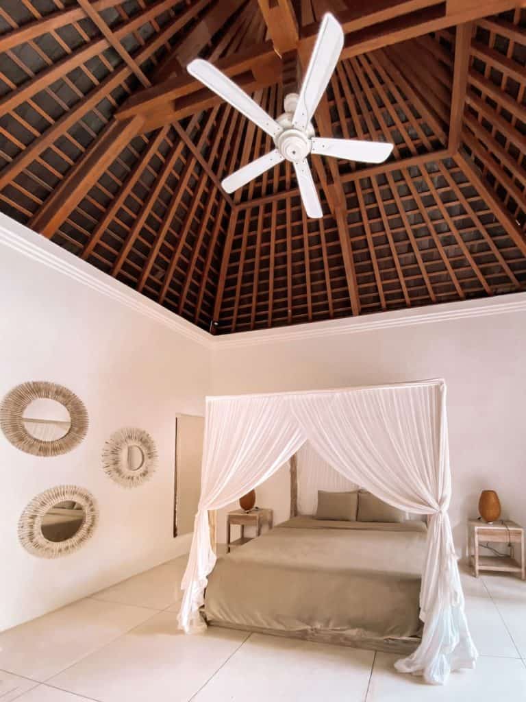 A large bed with a canope over it, mirrors on the wall, a very tall ceiling with a ceiling fan