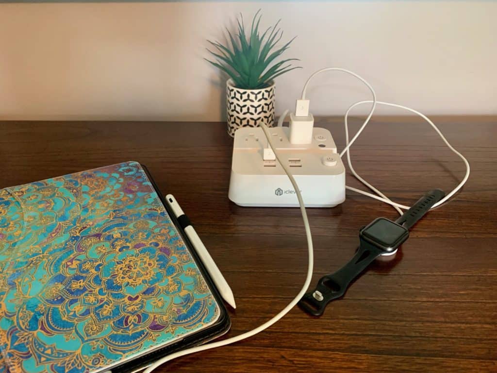 An ipad and apple watch charger in a travel power strip on a brown desk. Also has a small succulent plant in the background.