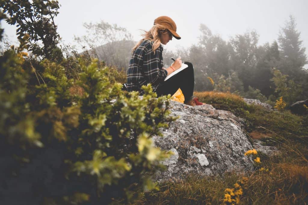 Woman sitting on a rock in nature writing in a journal