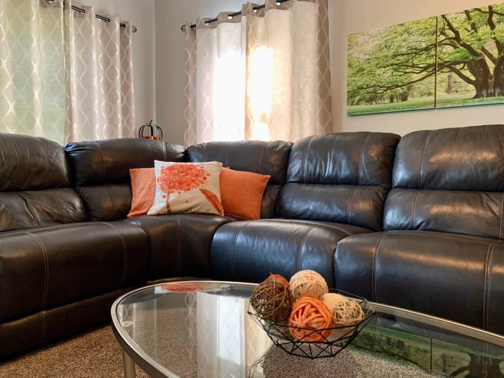 Cozy home decor with a couch with fall pillows, closed grey curtains behind and decorative bowl on a glass table