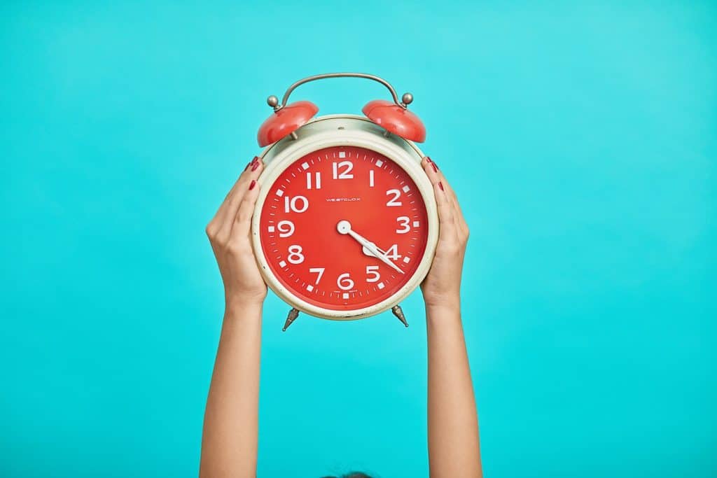 person holding red and beige twin bell analog alarm clock to master time blocking method