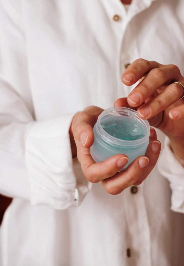 person holding blue plastic container for a skincare routine at home