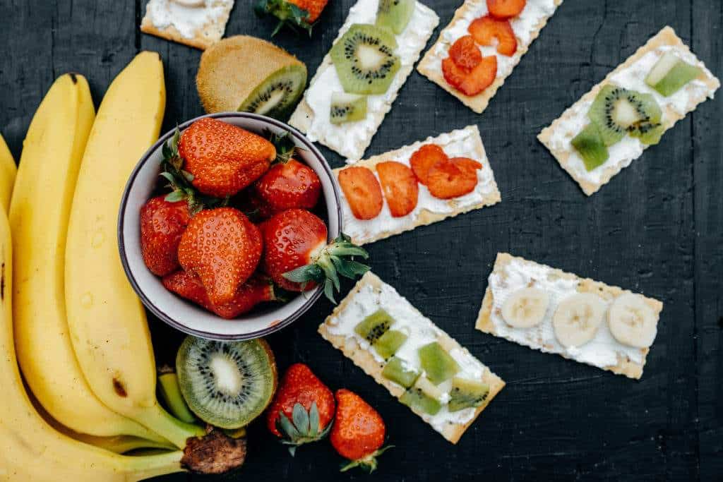 Crackers with cheese and fruits: bananas, strawberries and kiwi on a black background
