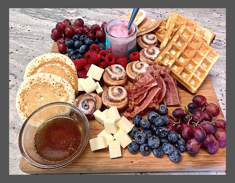 Easy Christmas breakfast ideas - breakfast charcuterie board with fruits, pancakes, waffles, bacon, fruit dip, cheese, pastries and syrup