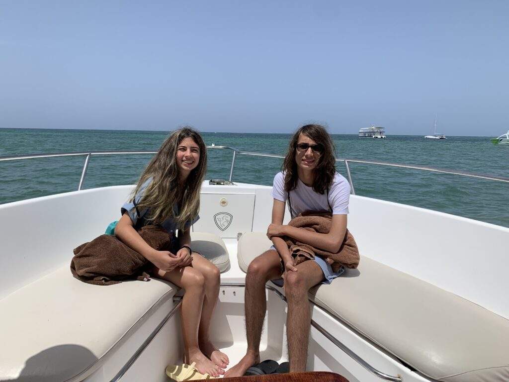 Two teenagers on a boat on a clear blue ocean.