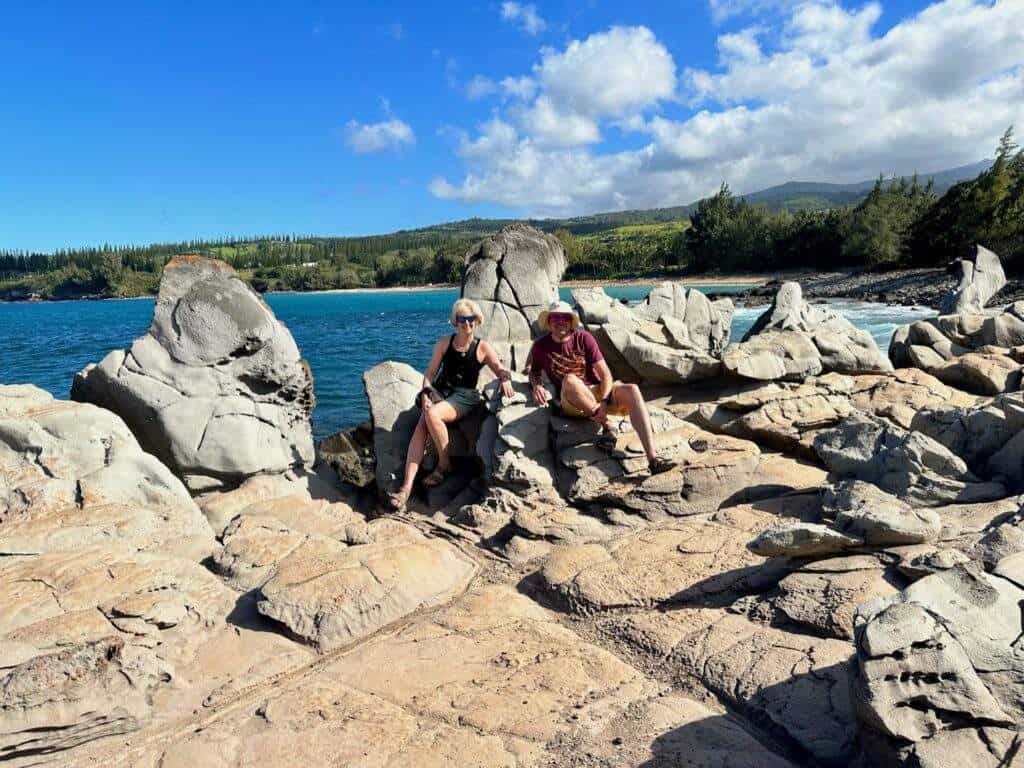 A man and a woman posing on rocks in front of an ocean bay in Maui