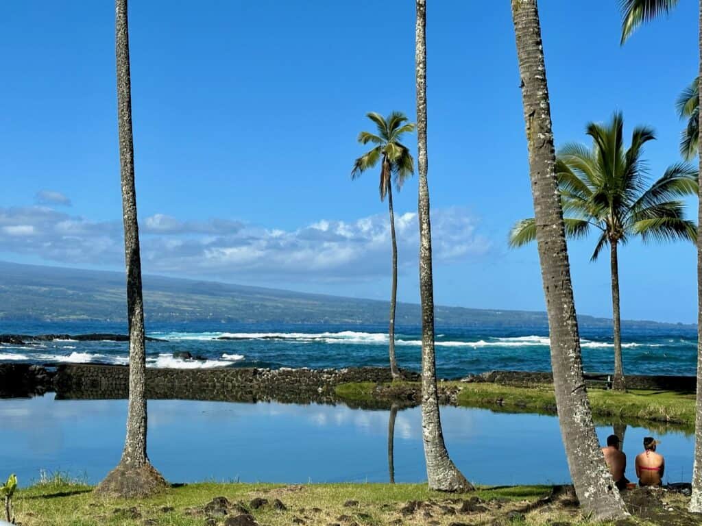 A calm pound, palms trees, two people and an ocean at Richardson Ocean park in Hilo Hawaii.