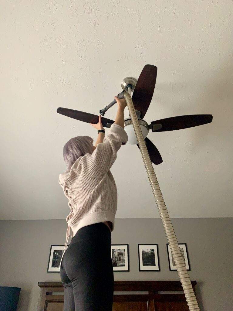 Woman cleaning a ceiling fan with a vacuum