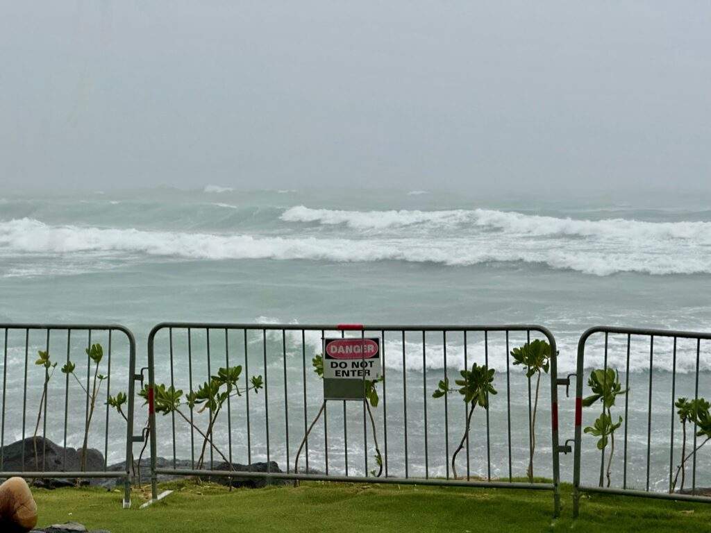What to do on the big island on a stormy day. Image of an ocean during a storm with a metal gate in front with a sign saying "danger. Do not enter:.