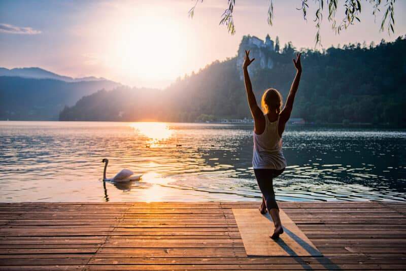 a woman practicing sun salutations by a lake at sunrise