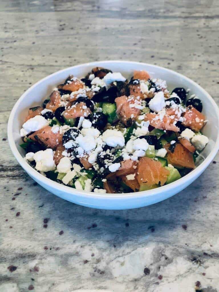 A picture of a healthy quinoa salad with smoked salmon, black olives, cucumbers, and feta cheese.