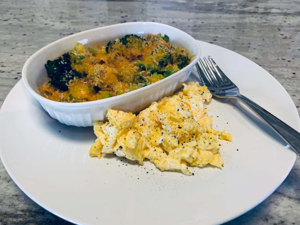 Scrambled eggs and a white ramequin of cheese quinoa and broccoli on a white plate.