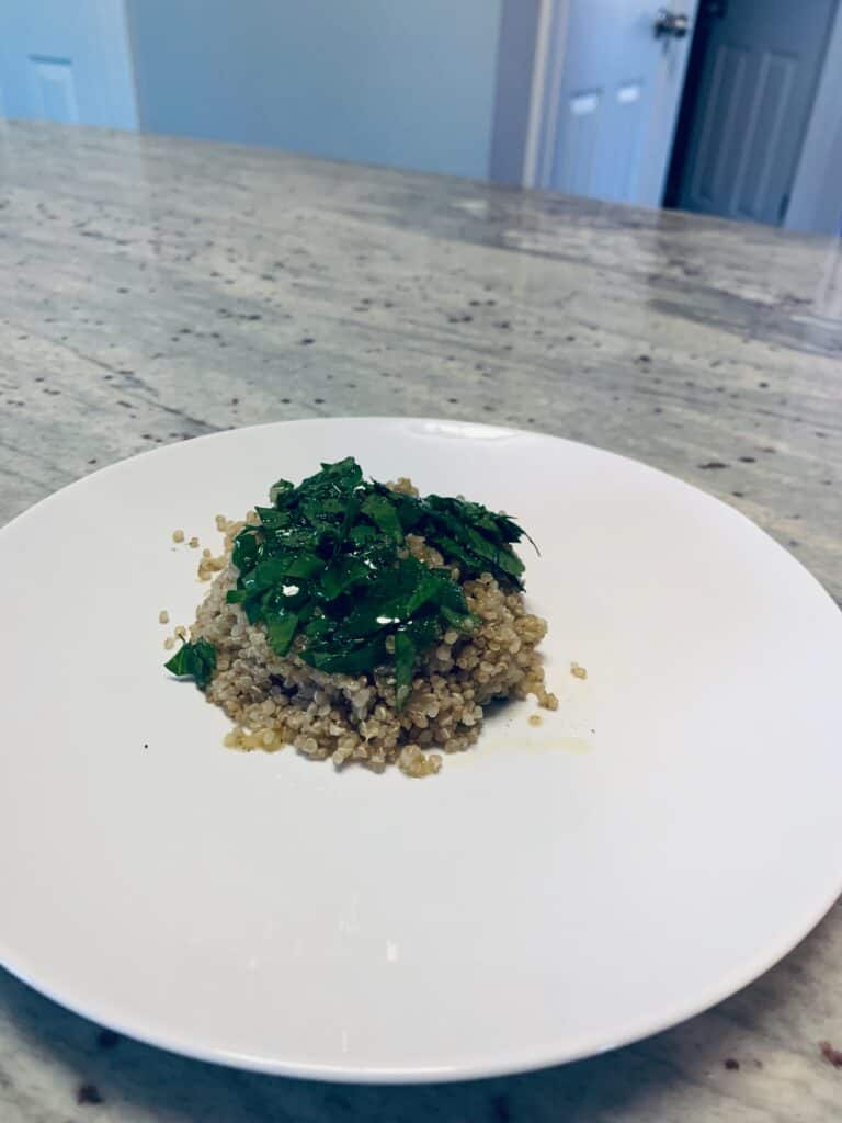 A quinoa cake with fresh herbs on top inside a white plate.