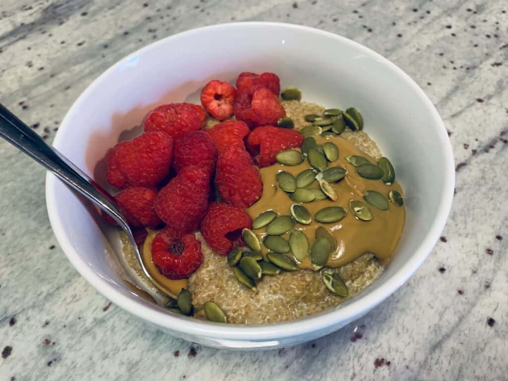 A healthy quinoa bowl with raspberries, sunflower butter and pumpkin seeds.