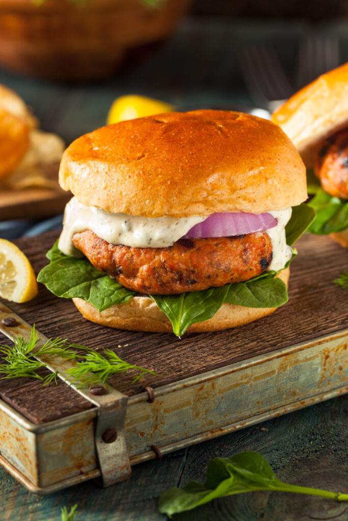 A gourmet salmon burger with tartar sauce, red onion, and fresh spinach. What a unique burger.