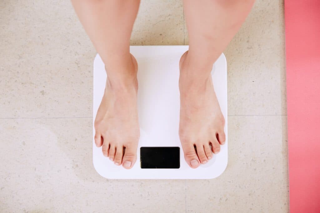 person standing on white digital bathroom scale. Is walking or running better for weight loss.