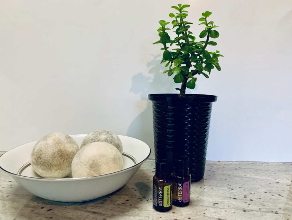 Wool drier balls in a white bowl with essential oil bottles and a bonsai tree
