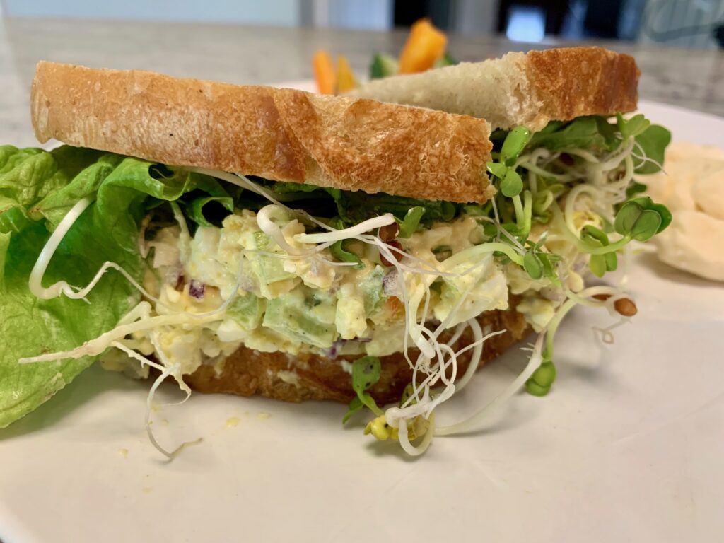 A delicious looking egg salad sandwich with sprouts and lettuce on sourdough bread