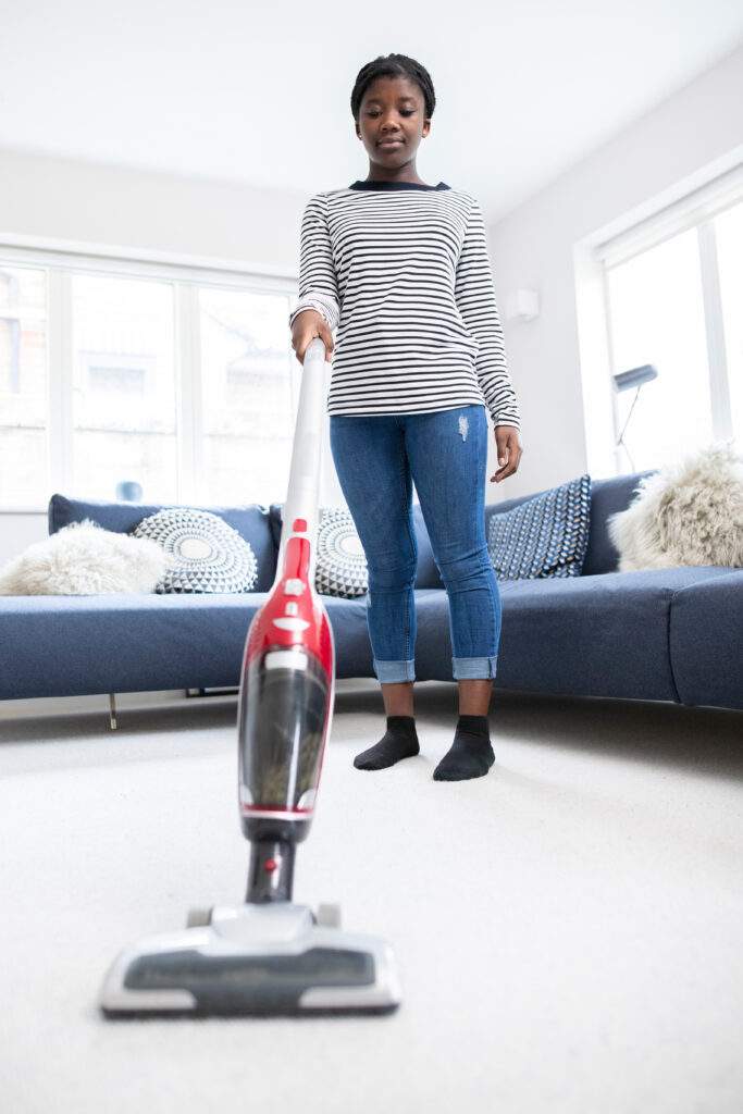 Teenage Girl Helping Out With Chores At Home Vacuuming Carpet In