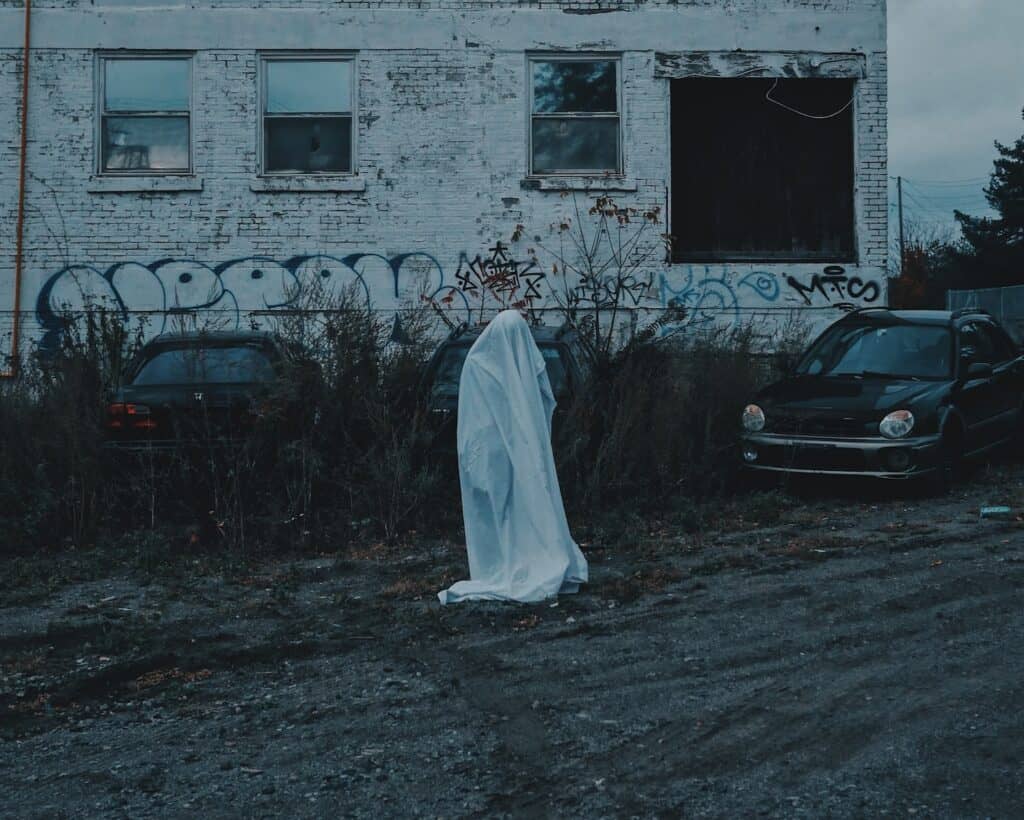 person standing in front of concrete building in ghost costume - fall destination ideas include haunted tours