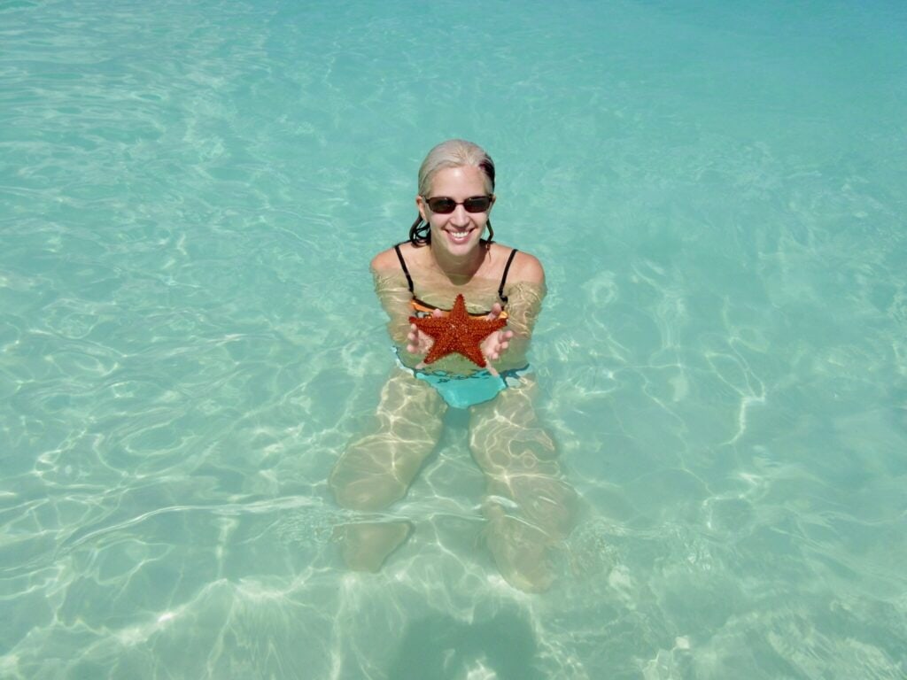 Woman holding a bright red star fish in Aruba at an all-inclusive resort