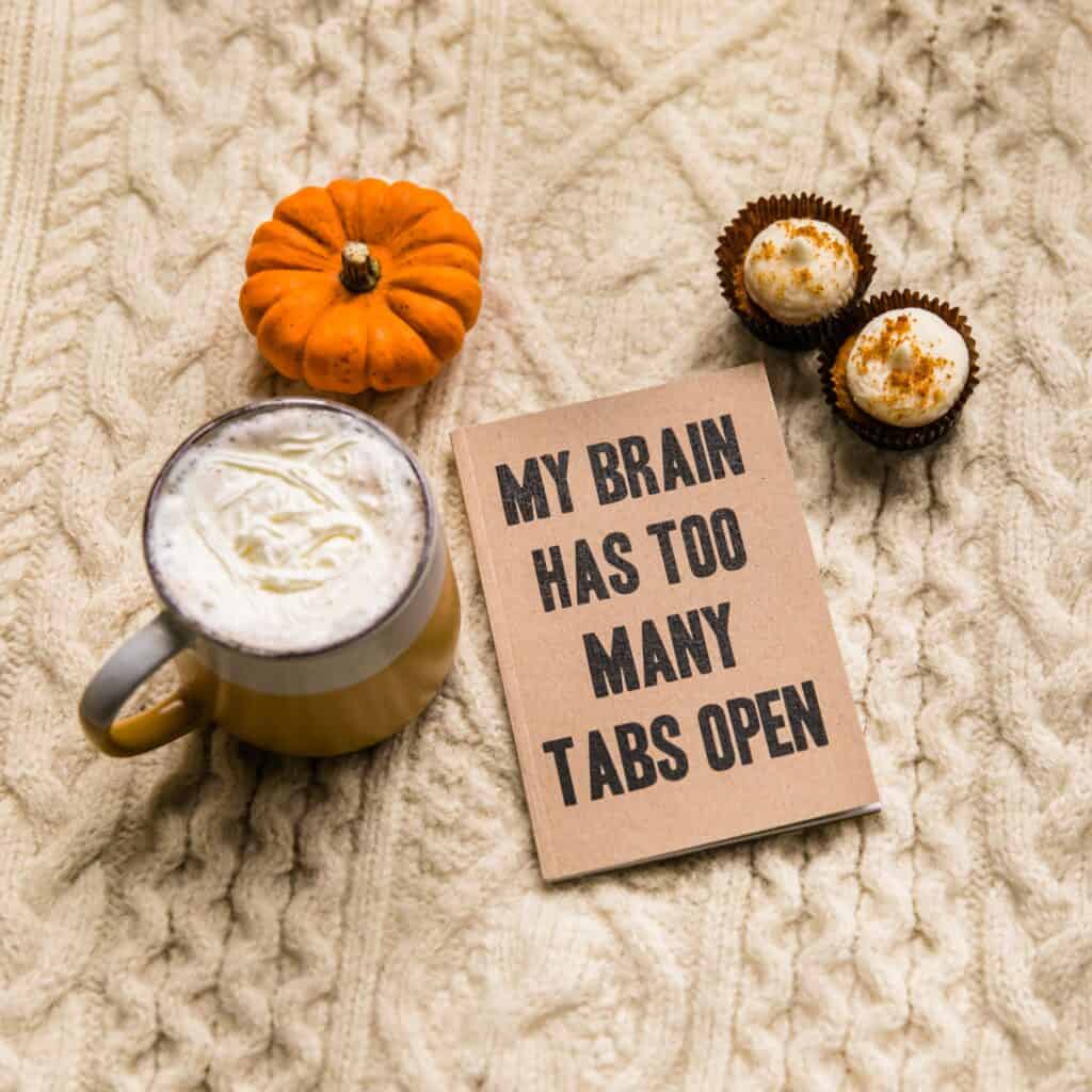 A sign that says my brain has too many tabs open with a cup of coffee, 2 cupcakes and a pumpkin