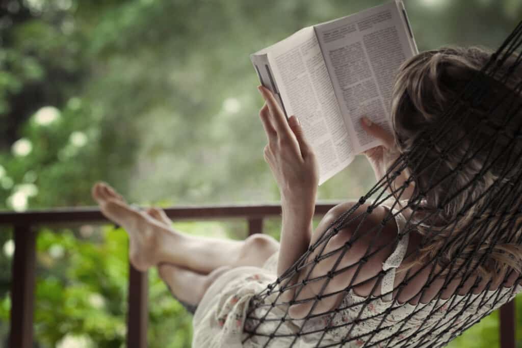 Woman lying in a hammock in a garden and enjoying a vacation book reading