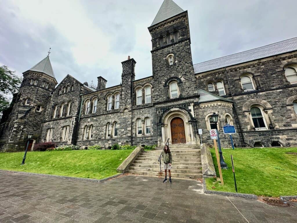 A gorgeous building in St George Campus with a young man standing in front of it.