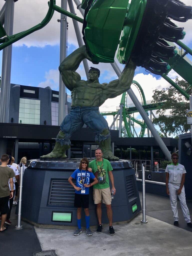A teenage boy and a man standing in front of a Hulk statue.