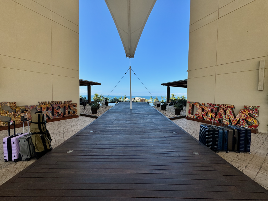 Signs with the names of 2 resorts with a ocean view in the background