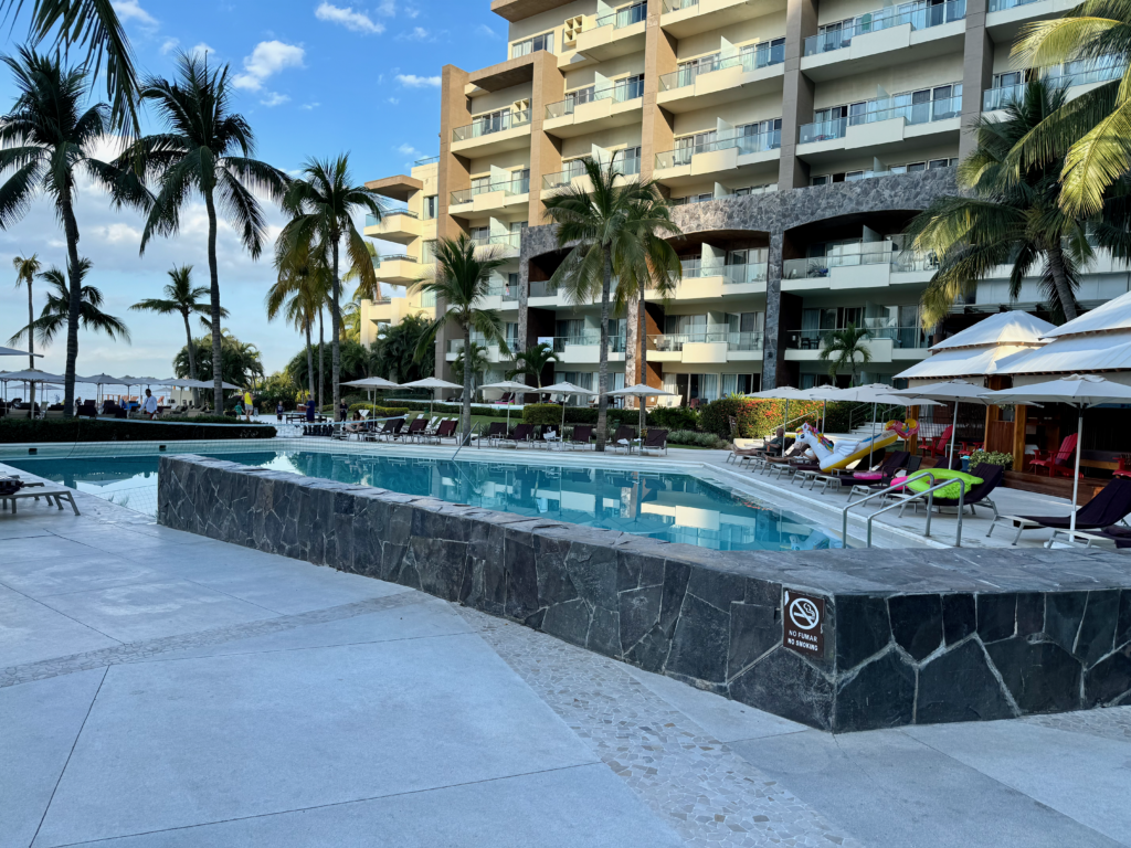 Image of a pool with palm trees and a building behind