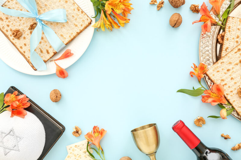 Frame made of flatbread matza, wine, Torah, kippah and alstroemeria flowers on color background