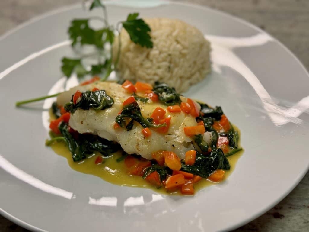 A piece of white fish sitting on top of spinach and red bell pepper with a side of rice and a spring of parsley as a Spring dinner