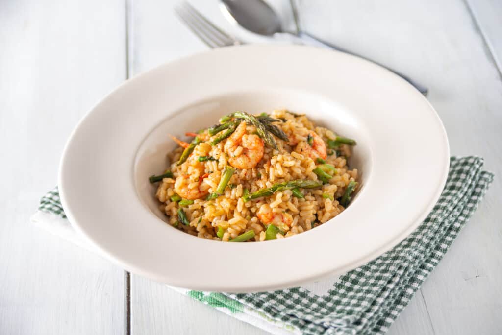 A white bowl sitting on a white table filled with shrimps and asparagus risotto