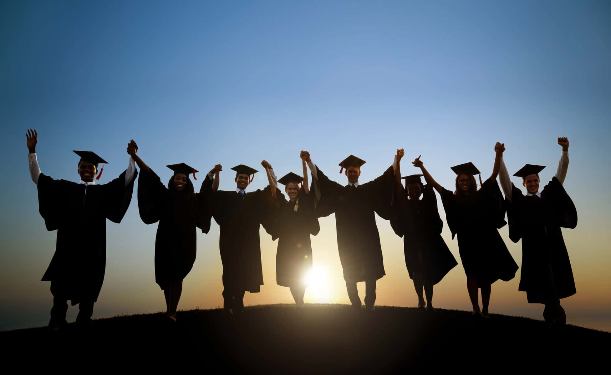 Photo of 8 high school graduate students in their caps and gowns at sunset.