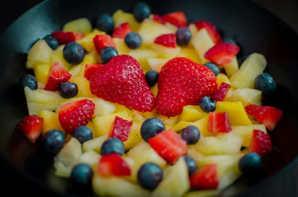 Seasonal fruit salad with red strawberries, pineapples, and blueberries on black ceramic bowl for a Mother's day brunch buffet