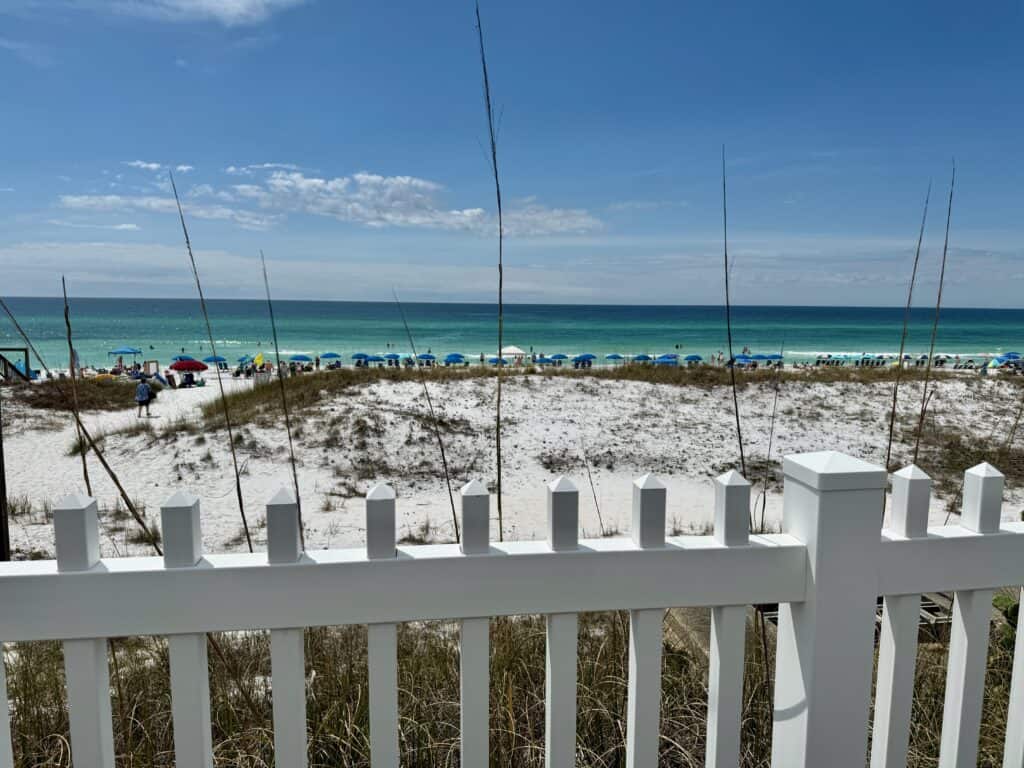 View of a beach and ocean across from a white picket fence.